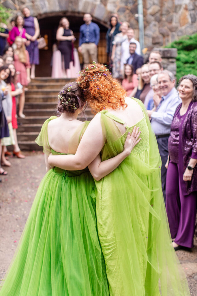 LGBTQ friendly wedding photographer Asheville capturing two brides in green gowns embracing during their ceremony exit surrounded by guests at Homewood