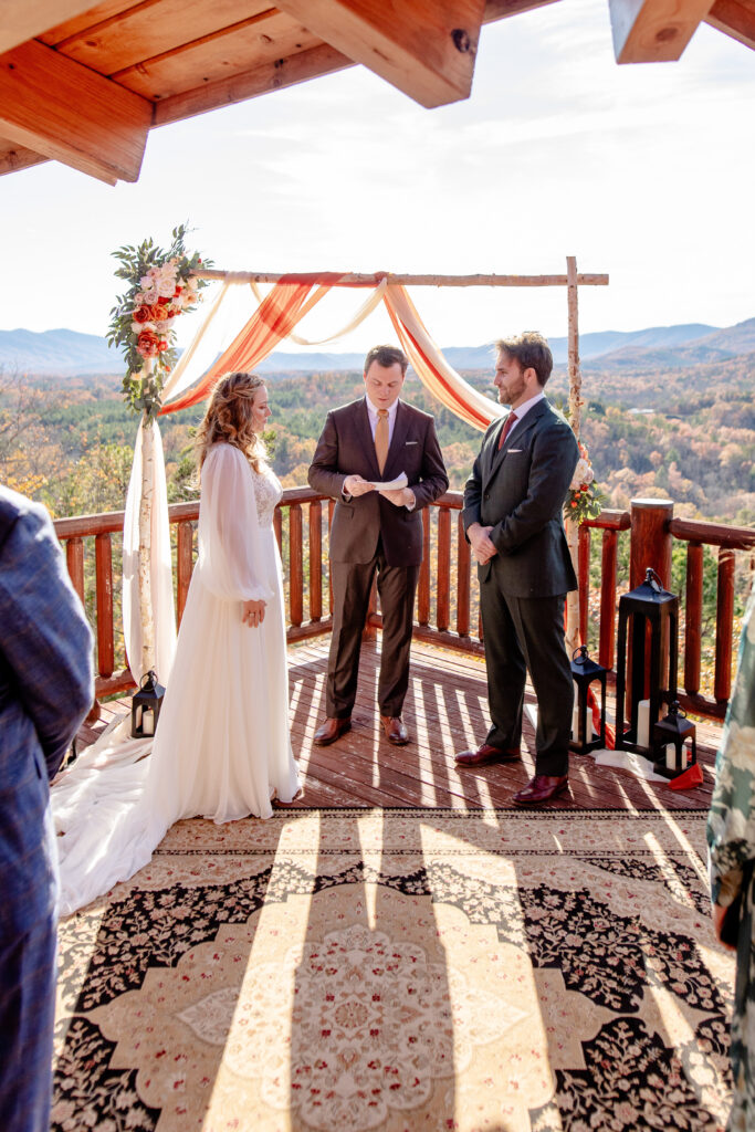 Asheville elopement ceremony on a cabin deck overlooking the Blue Ridge Mountains with a couple exchanging vows under a floral arch