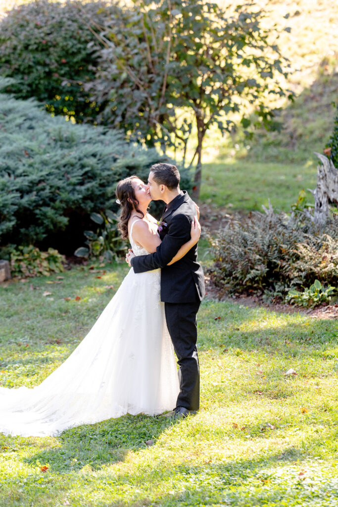 Bride and groom kissing during their Asheville elopement in a sunlit garden surrounded by Blue Ridge Mountain scenery