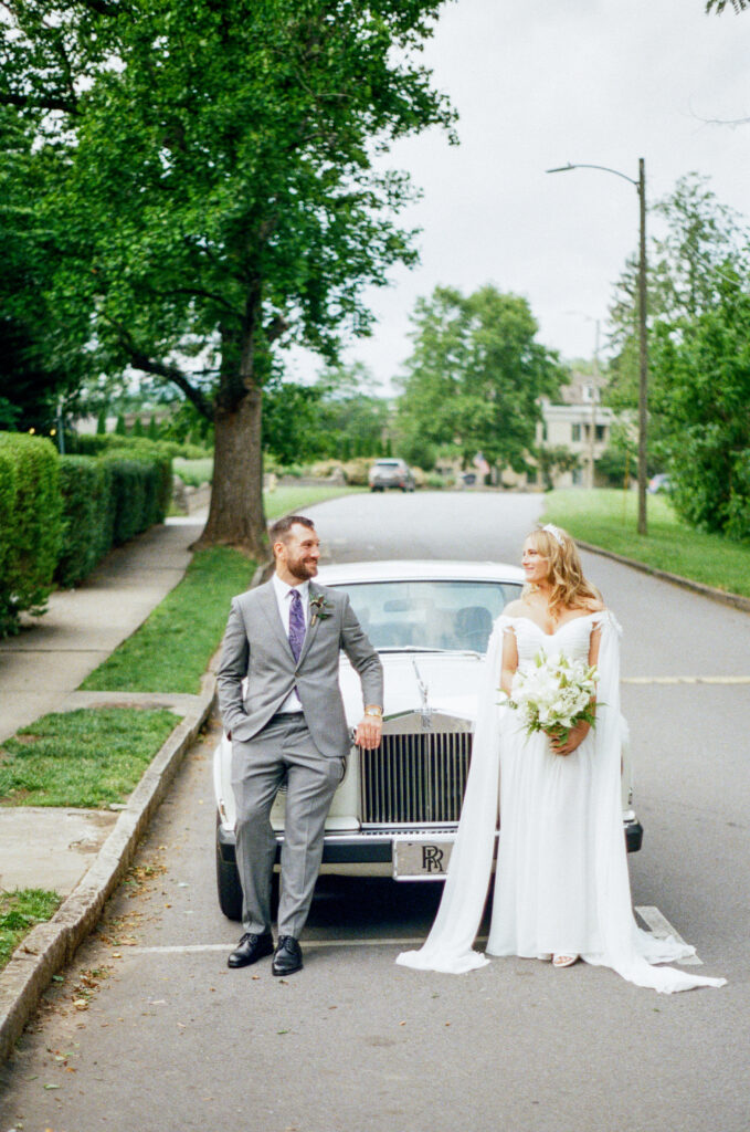 Bride and groom leaning into each other in front of a classic Rolls Royce during a Homewood wedding in Asheville, captured on film.
