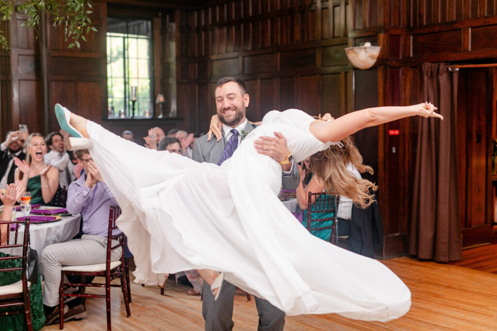 Groom lifting bride during wedding reception at Homewood in Asheville, captured mid celebration in the historic indoor space