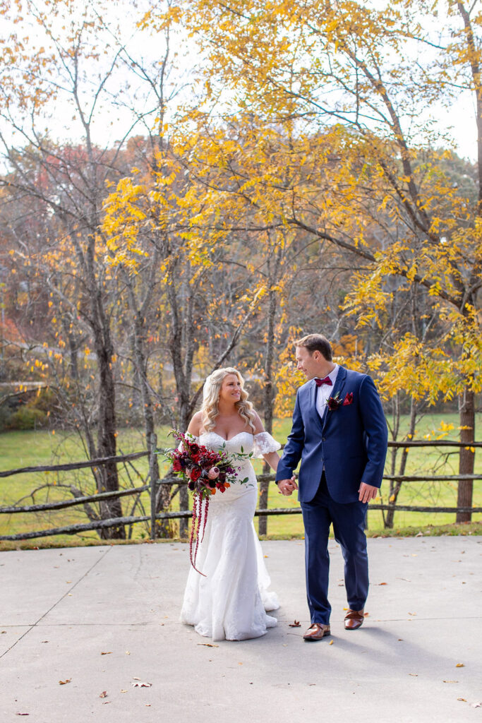 Bride and groom walking hand in hand during fall wedding portraits at Honeysuckle Hill wedding venue in Asheville, surrounded by golden leaves and countryside views