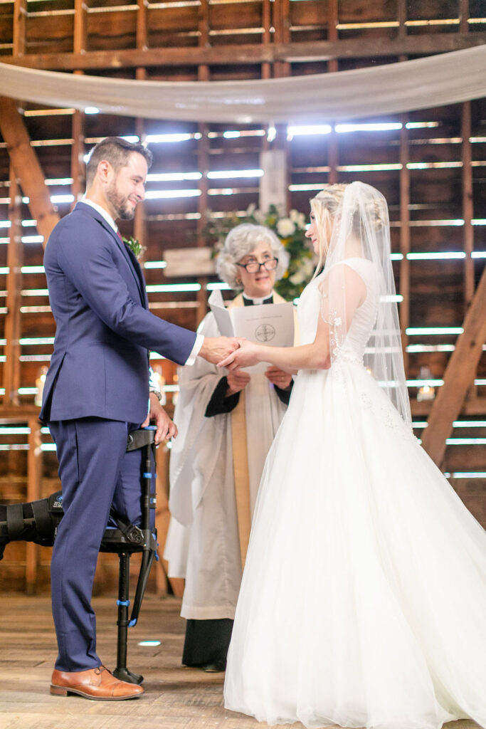 Bride and groom holding hands during their Honeysuckle Hill wedding ceremony inside the rustic barn with natural light and wooden backdrop