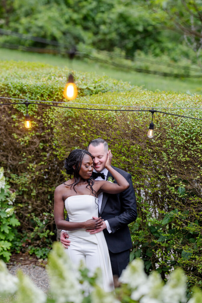 bride and groom embracing in a lush garden with string lights during their Asheville NC wedding