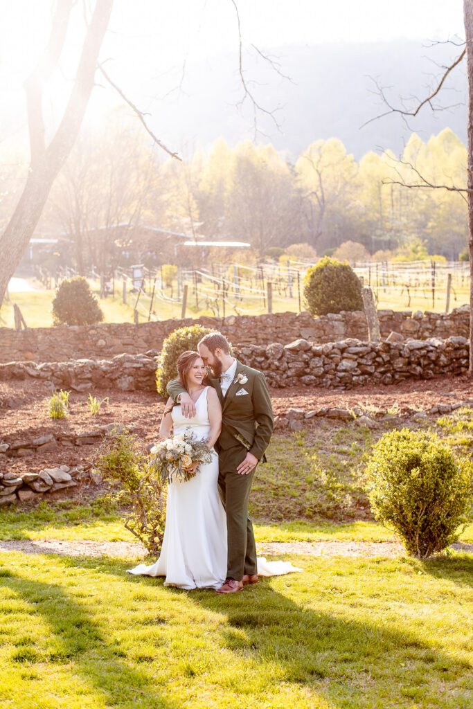 bride and groom laughing together in a garden with stone walls and glowing spring light at an Asheville NC wedding venue