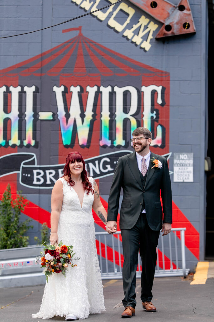 bride and groom holding hands and smiling in front of the Hi-Wire Brewing sign at their Asheville NC wedding