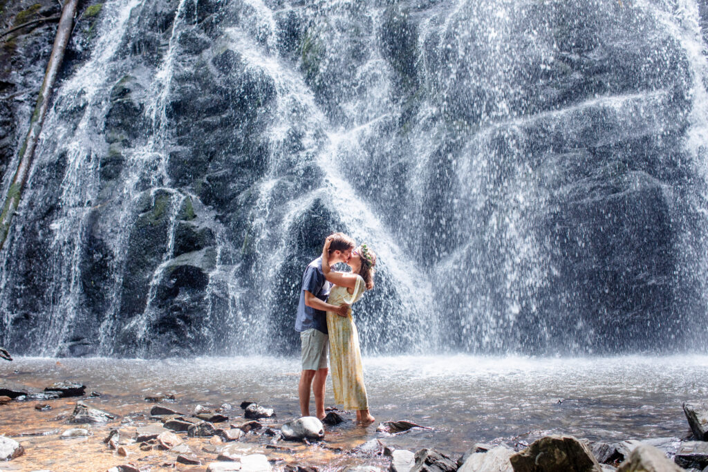 couple kissing in front of a waterfall in the mountains near Asheville NC during their engagement session