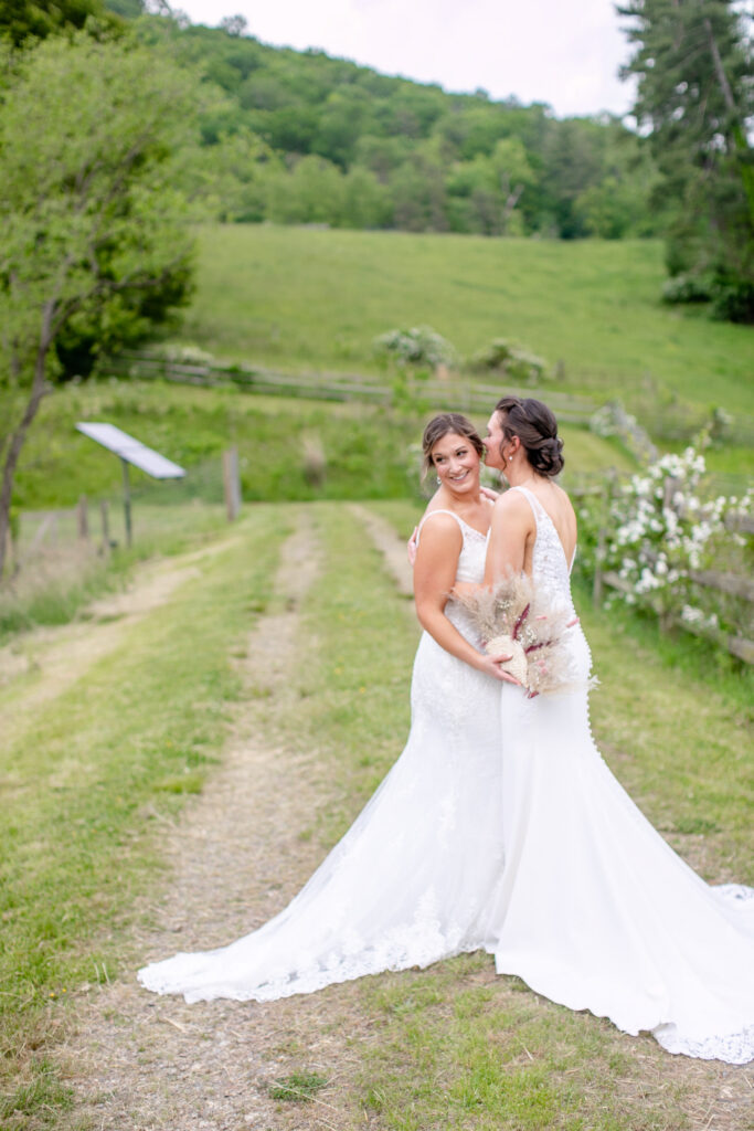  two brides laughing together on a farm lane with green mountain views at an Asheville NC same sex wedding

