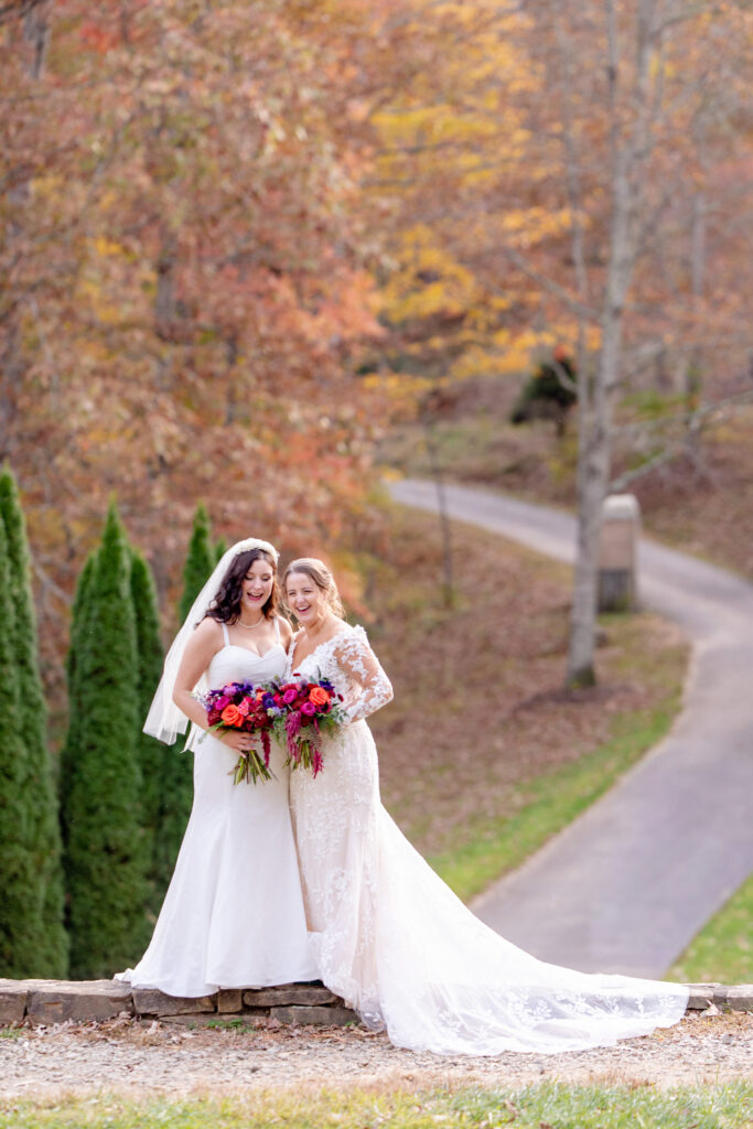 
two brides standing together with colorful bouquets surrounded by fall foliage at an Asheville NC same sex wedding