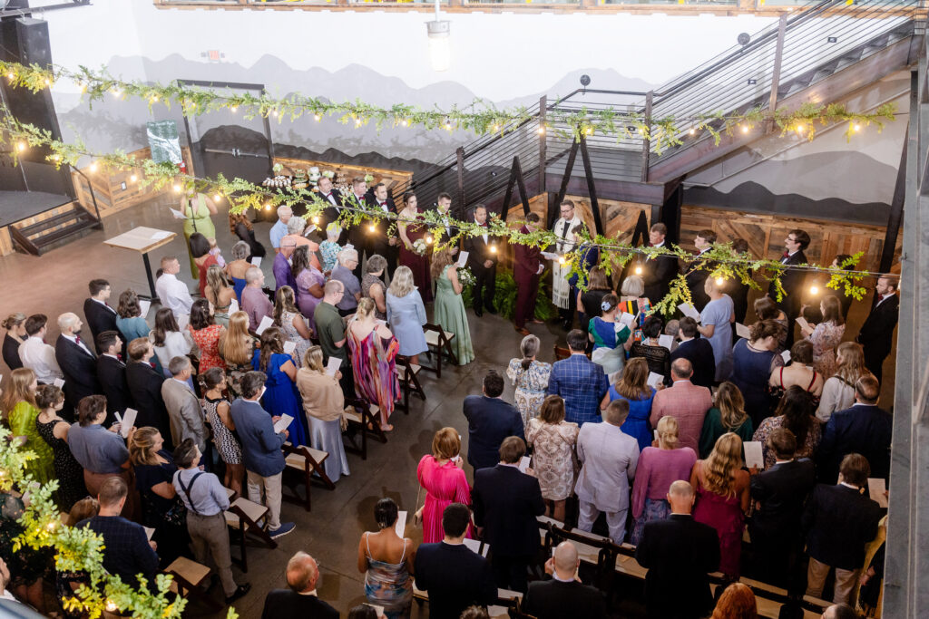 aerial view of indoor wedding ceremony at Highland Brewing Company Event Center in Asheville NC with string lights and greenery garland