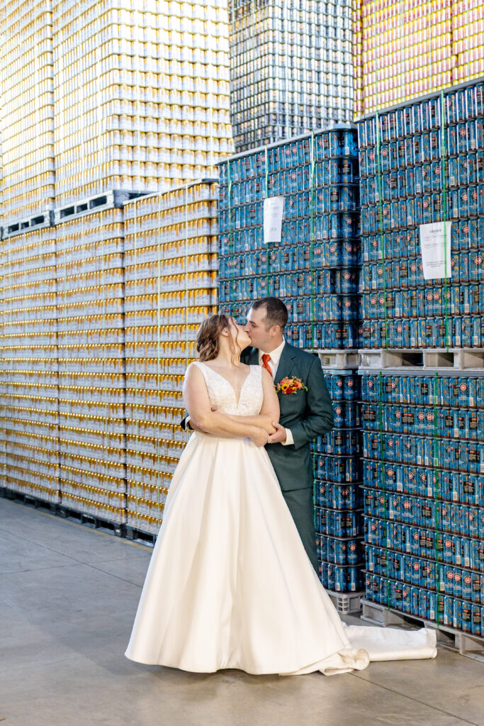 bride and groom kissing in front of stacked beer cans at Highland Brewing Company wedding in Asheville NC