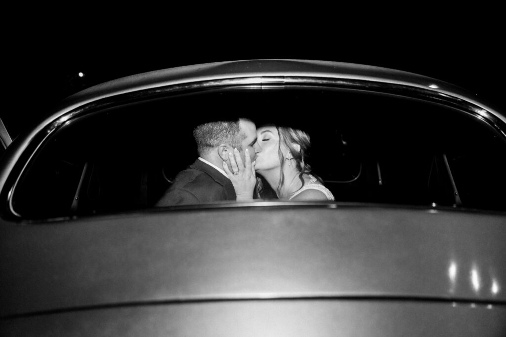 black and white photo of bride and groom kissing through car window at end of Highland Brewing wedding night in Asheville NC