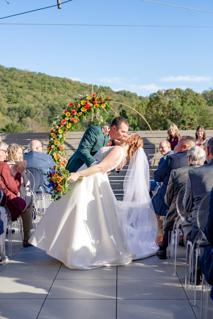 bride and groom first kiss during fall rooftop wedding ceremony at Highland Brewing Company in Asheville NC