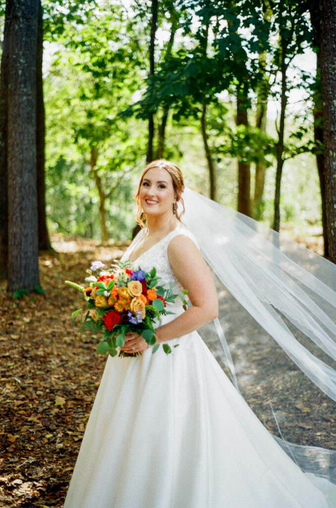 bride with flowing veil and colorful bouquet in the wooded meadow at Highland Brewing Company wedding in Asheville NC