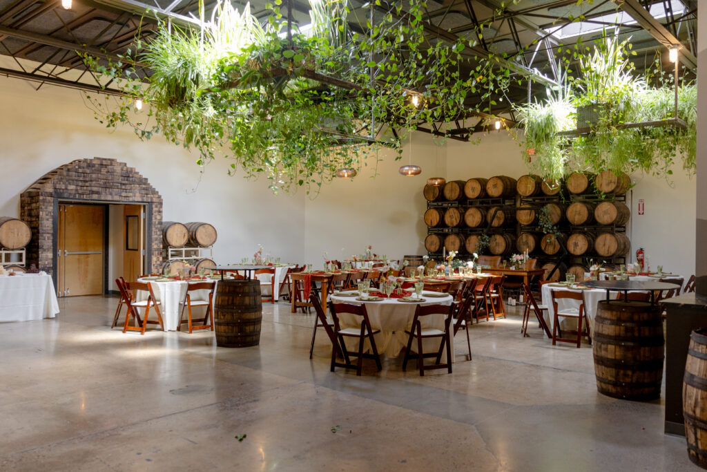 Barrel Room wedding reception setup at Highland Brewing Company in Asheville NC with hanging greenery, barrel racks, and round tables